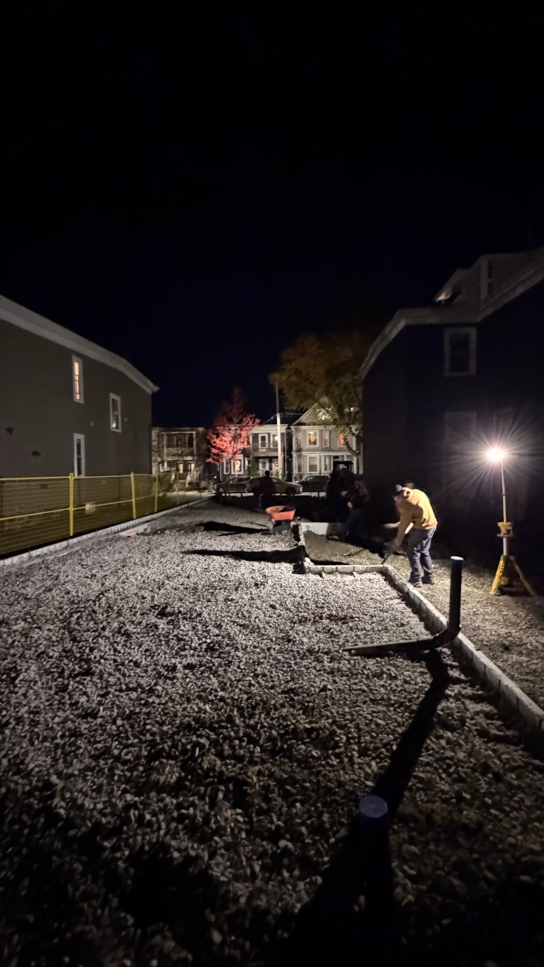 Evening hardscaping work raking gravel for a new driveway by floodlight