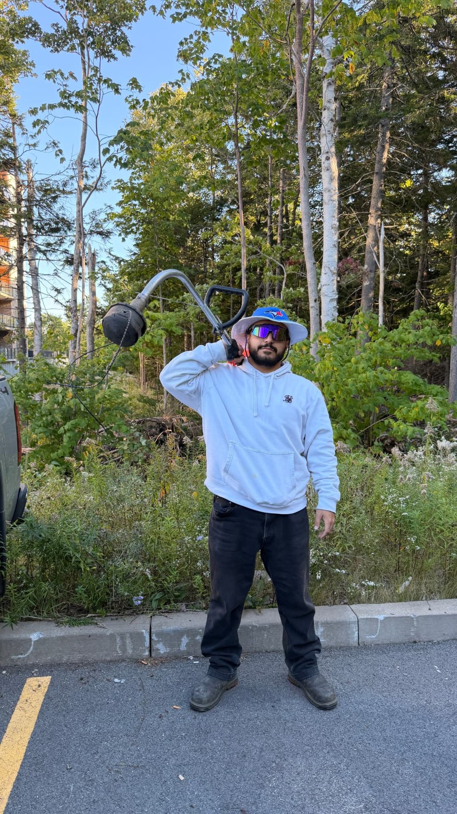 Kass carrying a grass trimmer beside a wooded property